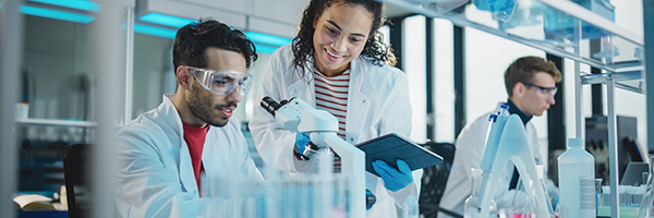 Modern Medical Research Laboratory: Portrait of Latin and Black Young Scientists Using Microscope, Digital Tablet, Doing Sample Analysis, Talking. Diverse Team of Specialists work in Advanced Lab
